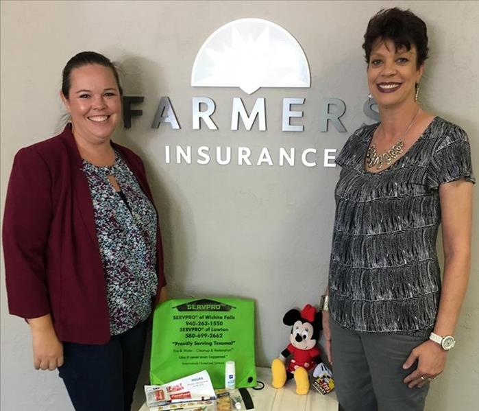 Two females standing by Farmers Insurance sign with Minnie Mouse toy on table