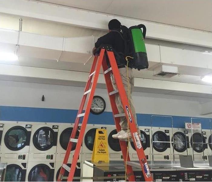 man on orange ladder cleaning ceiling